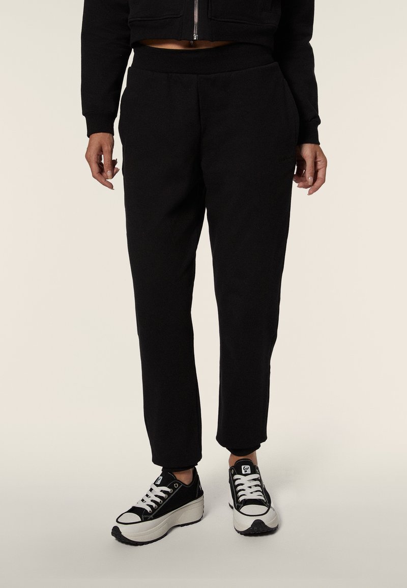 Pantalones sudaderos negros con un ajuste relajado, que cuentan con una cintura elástica, bolsillos laterales y piernas cónicas, combinados con zapatillas en blanco y negro.