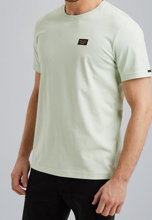 T-shirt en coton vert clair avec un col rond, des manches courtes et une petite étiquette noire sur la poitrine ; texture lisse, coupe ajustée.