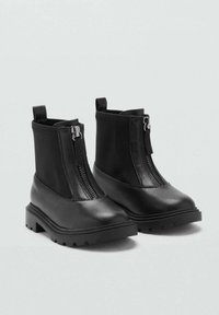 Botines negros de piel sintética con cremallera frontal, tirador en la parte trasera, suela gruesa y textura suave.