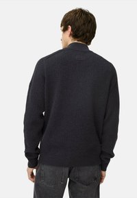 Dunkelblaues, geripptes Strickpullover mit langen Ärmeln und einem kragenähnlichen Hals. Hat ein dezentes Muster und wird mit dunkelgrauen Jeans kombiniert.
