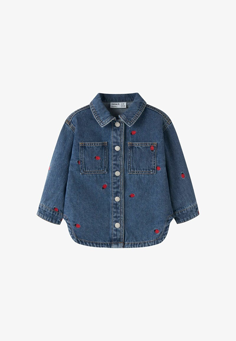 Veste en denim bleu pour enfants à boutons avec deux poches poitrine et des motifs de coccinelles rouges brodés dispersés sur le tissu.