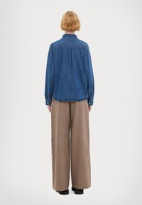 Τζιν πουκάμισο με γιακά, μακριά μανίκια και άνετη εφαρμογή. Συνδυασμένο με ανοιχτό καφέ παντελόνι σε φαρδιά γραμμή και μαύρα παπούτσια.