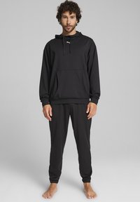 Sort pullover hoodie med en forlommes, snoretræk i hætten og logo. Kombineret med matchende smalle sweatpants, begge lavet af et blødt stof.