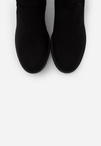 Botas de tobillo de ante negro con puntera redondeada y suela de goma texturizada. El diseño superior presenta un acabado suave sin adornos.