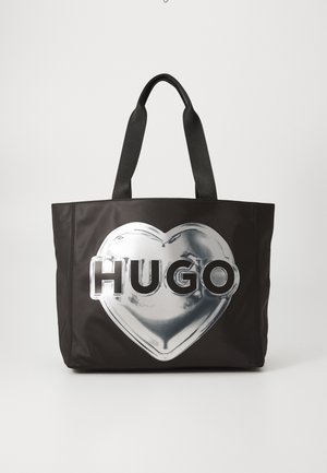 Czarna torba na ramię wykonana z materiału syntetycznego, z dużym wzorem srebrnego serca z tekstem "HUGO" w wyraźnych literach. Solidne czarne uchwyty.