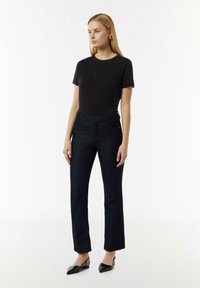 Zwarte t-shirt met korte mouwen en reliëftekst op de voorkant, gecombineerd met donkere denim hoge taille rechte jeans en zwarte slingback schoenen.