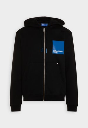Felpa nera con zip realizzata in tessuto morbido, dotata di una tasca quadrata blu e accento con logo. Comprende cappuccio con cordino e tasche frontali.