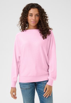 Light pink sweater with a wide neckline, long sleeves, and ribbed cuffs. Paired with blue jeans, it features a relaxed fit and smooth texture.