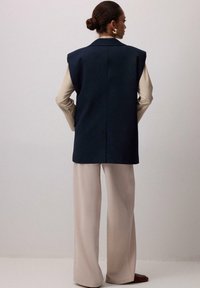 Námornícky bezrukávový blejzer so štruktúrovaným dizajnom, kombinovaný s svetlo béžovými nohavicami so širokými nohavicami. Hladká textília s lešteným povrchom.