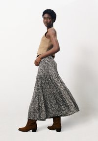 Bruine mouwloze top, zwart-witte maxi rok met bloemenpatroon, gestructureerde stof, kniehoge bruine suède laarzen met een blokhak.