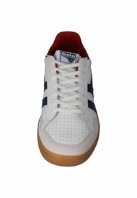 White sneaker with navy blue stripes, red inner lining, perforated toe, white laces, and brown gum sole, front view.