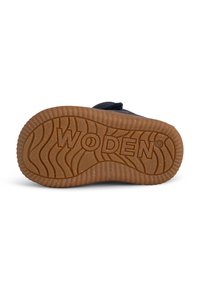 Suela negra de un zapato con un patrón texturizado y ondulado, que presenta el nombre de la marca "WODEN" prominentemente grabado en el centro.