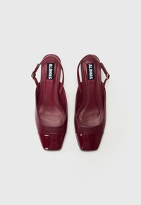 Saltos slingback em pele patinada burgundy com bico quadrado, apresentando um acabamento suave e uma fivela em tom dourado na tira do tornozelo.