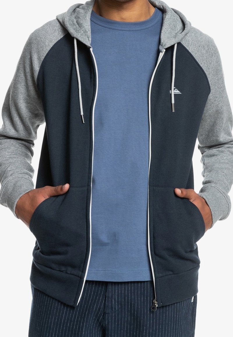 Navy and gray hooded sweatshirt with zipper, two front pockets, and white drawstrings. The left shoulder features a small logo.