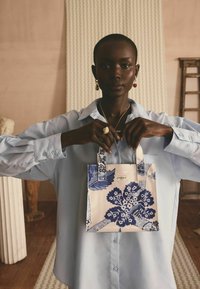 Mazs, rakstains iepirkumu soma zilos un baltos toņos ar ziedu ornamentiem. Izgatavota no auduma ar strukturētu formu un īsām rokturām.