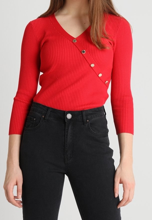 Czerwony prążkowany top z długim rękawem, dekoltem w serek i ukośnym zdobieniem na guzikach. Połączony z czarnymi, wysokim stanem jeansami. Gładka tekstura, dopasowany krój.