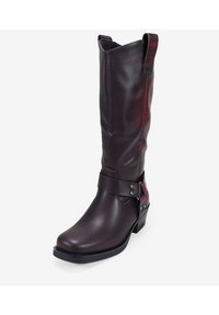 Bota de vaquero de cuero marrón con un tronco alto, costuras en contraste, correa decorativa con acentos metálicos y un tacón bajo y apilado.