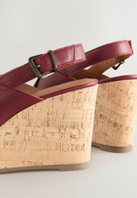 Burgundske usnjene slingback klini s pluto platformo. Imajo zaponko in teksturirano pluto površino na peti.