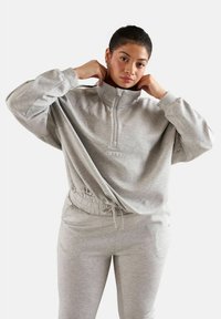 Harmaa fleece-tekoturkki, jossa on korkea kaulus ja joustava vyötärö. Yhdistetty harmaisiin verkkareihin. Yksinkertainen, rento muotoilu.