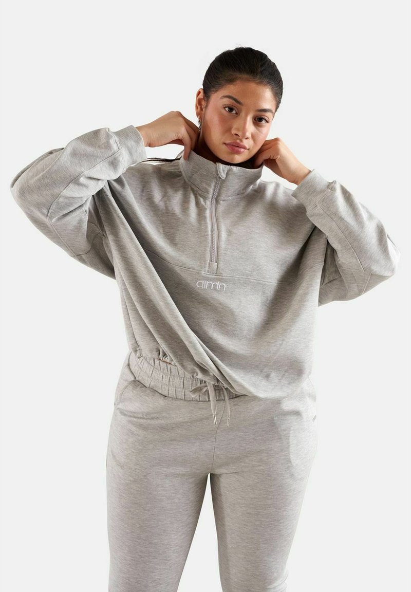 Harmaa fleece-tekoturkki, jossa on korkea kaulus ja joustava vyötärö. Yhdistetty harmaisiin verkkareihin. Yksinkertainen, rento muotoilu.