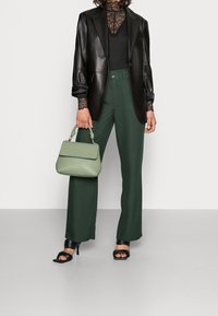 Svart läderblazer över en spets-topp, tillsammans med gröna vida byxor. En texturerad grön handväska och svarta högklackade sandaler fulländar looken.