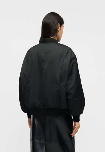 Fekete bombázó dzseki sima, könnyű anyagból, bordázott gallérral és mandzsettával, laza, túlméretezett szabással. Látható fémalkatrész vagy minta nélkül.