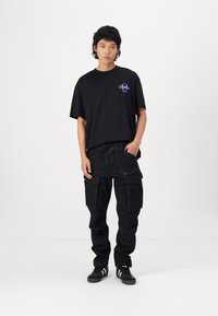 Black cotton t-shirt with a small blue logo on the chest, paired with dark blue cargo pants featuring multiple pockets and zippers.