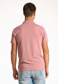 T-shirt i kort ärm i mjuk rosa tyg, med en standardkrage och slät yta, visad från baksidan med ljusblå jeans.