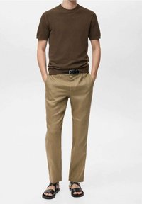 Maglione corto a maniche corte marrone, pantaloni beige a pieghe e sandali neri. Design semplice, tessuto leggero e vestibilità rilassata.