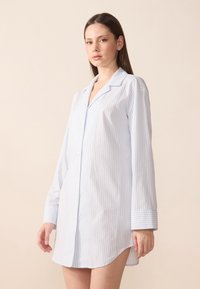 Camicia button-up a righe azzurre e bianche con maniche lunghe e colletto. Presenta un orlo curvo e maniche con polsini.