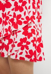 Falda floral con fondo blanco, grandes flores rojas y hojas verdes. La tela es ligera y tiene un dobladillo con volantes.