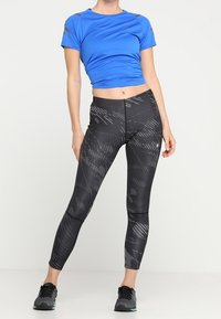 Modrý sportovní top s krátkými rukávy a šedými detaily, kombinovaný s černými legínami s vysokým pasem a strukturovaným geometrickým vzorem.