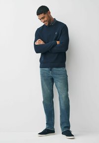 Granatowy sweter o prążkowanej fakturze z okrągłym dekoltem, w połączeniu z jasnoniebieskimi dżinsami i ciemnymi trampkami, charakteryzujący się luźnym krojem i subtelnym logo.