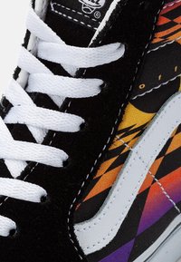 Black suede sneaker with white laces, featuring a multicolor geometric pattern in orange, purple, and black on the side. White leather accents.