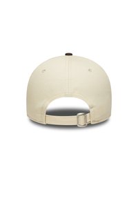Gorra de béisbol color crema con forma redondeada, correa ajustable y un botón de tela oscura en la parte superior. Presenta agujeros de ventilación.
