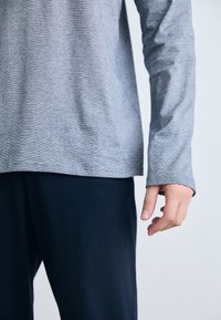 Camisa gris de manga larga con una sutil textura a rayas, combinada con pantalones azul marino oscuros. Presenta un corte relajado y cuello redondo.
