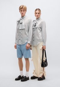 Ριγέ πουκάμισα με κουμπιά και μεγάλες παπιγιόν, σορτς από τζιν και κρεμ παντελόνια με λεπτομέρειες από κορδέλα. Μαύρα παπούτσια και τσάντα ολοκληρώνουν την εμφάνιση.