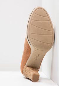 Chaussure à talons en daim marron avec une semelle en liège. Présente une pointe lisse et arrondie ainsi qu'une semelle en caoutchouc texturée.
