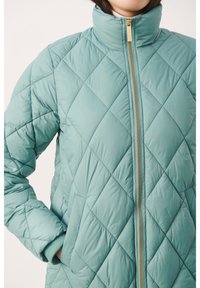 Chaqueta acolchada verde menta con un alto cuello, cremallera dorada y puños acanalados. Presenta un patrón de diamantes y bolsillos laterales.