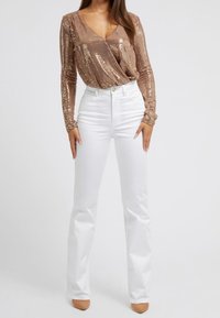 Long-sleeve, V-neck top in shiny rose gold sequins paired with high-waisted white flared pants, featuring button closure and classic pockets.