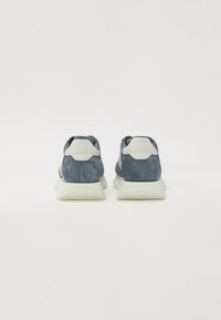 Baskets en suede bleu avec des accents blancs, dotées d'une semelle épaisse, d'un design incurvé et d'un onglet de talon texturé. La vue arrière montre les détails de laçage et de rembourrage.