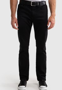 Jeans de mezclilla negros con un corte slim, diseño de cinco bolsillos y detalles de costura sutiles; llevados con un cinturón negro y zapatillas negras.