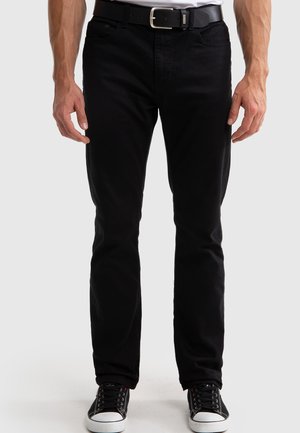 Crne traperice slim fit kroja, s pet džepova i suptilnim detaljima šivanja; nosi se s crnim remenom i crnim tenisicama.