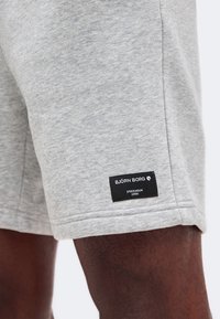 Κοντινή λήψη γκρι σορτς heather σε άτομο, που εμφανίζει μια μαύρη ετικέτα με το κείμενο "BJÖRN BORG Stockholm 1956" στο κάτω τελείωμα.