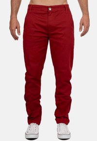 I pantaloni in cotone rossi presentano una vestibilità slim, tasche anteriori e una chiusura con bottone. Abbinati a sneakers bianche per un contrasto.