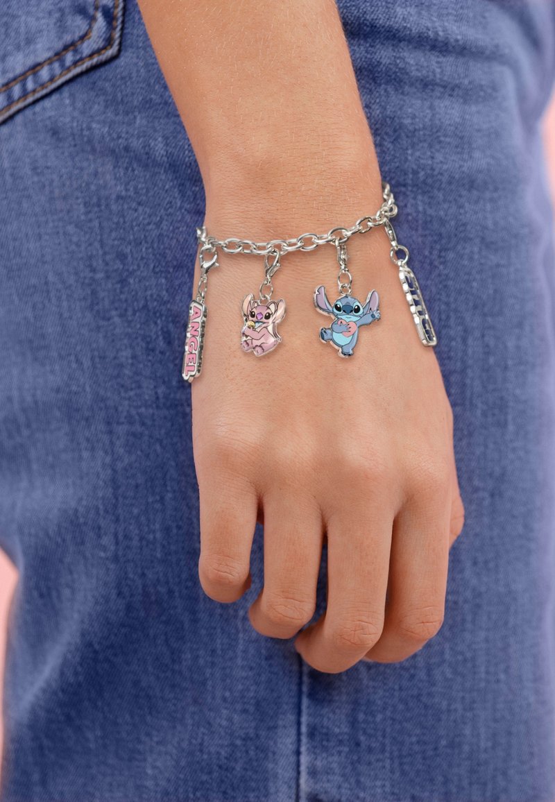 Zilveren kettingarmband met twee kleurrijke emaille bedels die cartoonfiguren afbeelden en een label met de tekst "ENGEL." Draagt op een met denim geklede pols.