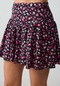 Blumiger Rock aus schwarzem Stoff mit rosa und weißen Blumen. Verfügt über ein ausgestelltes Design und einen Rüschensaum für Bewegung und Stil.