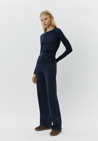 Jūras spēku garām piedurknēm krekls ar smalkām svītrām, apvienots ar platām jūras spēku biksēm un brūnām apaviem. Vienkāršs dizains ar pieguļošu siluetu.