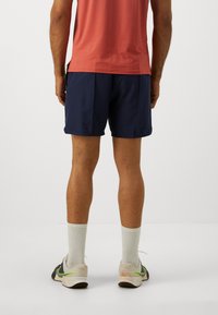 Navy athletic shorts with a lightweight design, paired with a coral shirt. White calf-length socks and multi-colored running shoes.