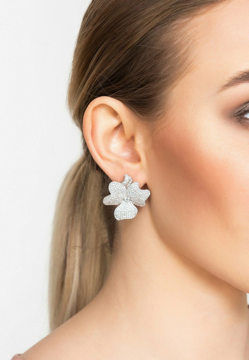 Pendientes de plata en forma de mariposa con una superficie texturada, que cuentan con tres pétalos y un diseño de racimo, llevados en una oreja.